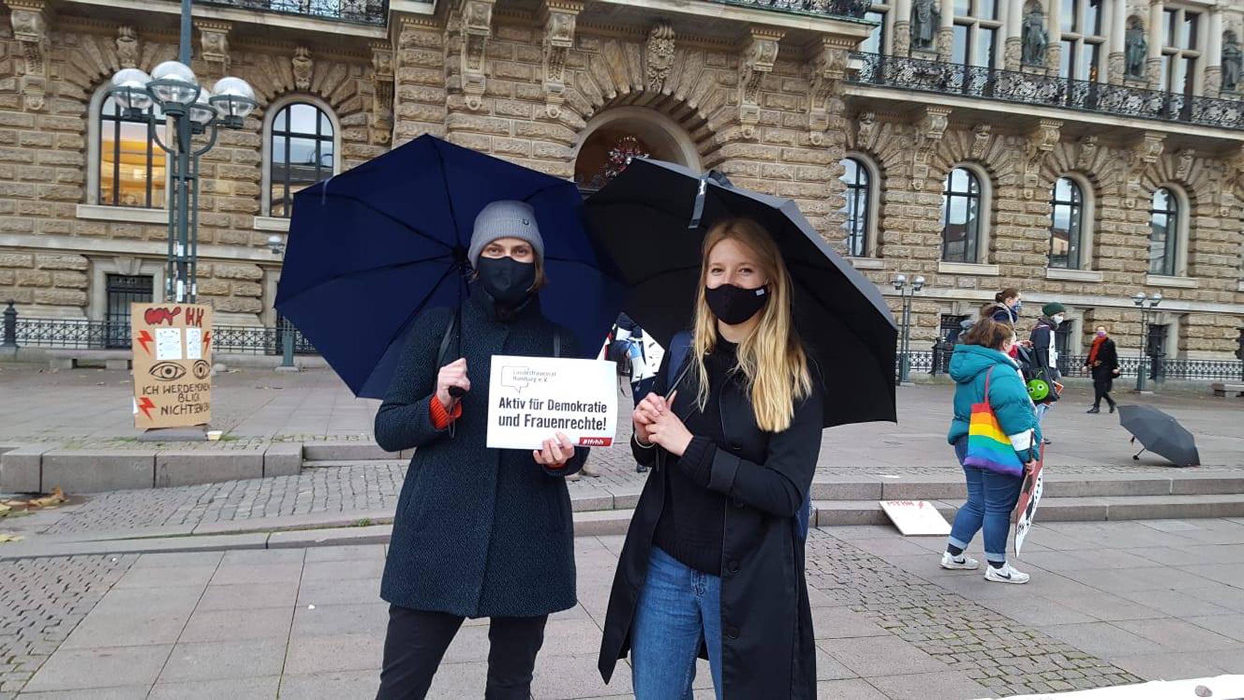 Zwei Personen stehen vor dem Hamburger Rathaus mit einem Demo-Schild.