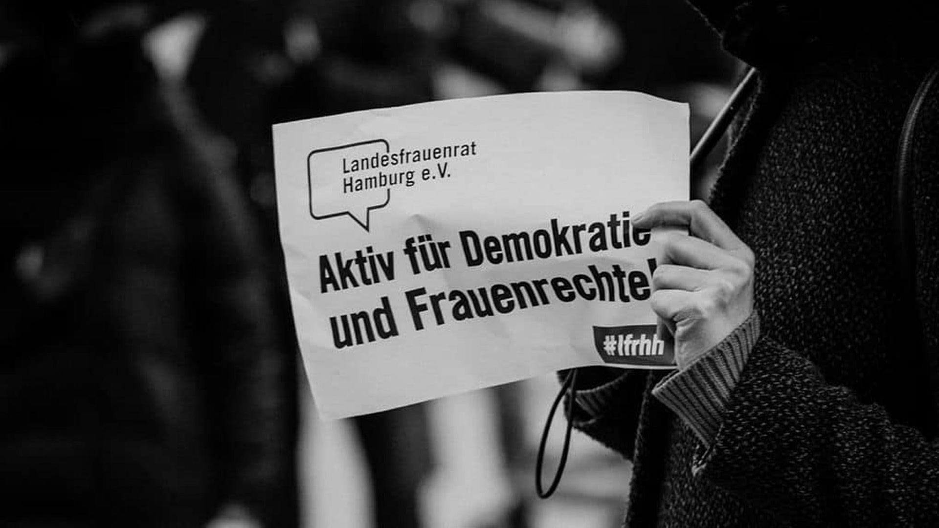 Person hält ein Schild hoch auf dem steht: Landesfrauenrat Hamburg, Aktiv für Demokratie und Frauenrechte!