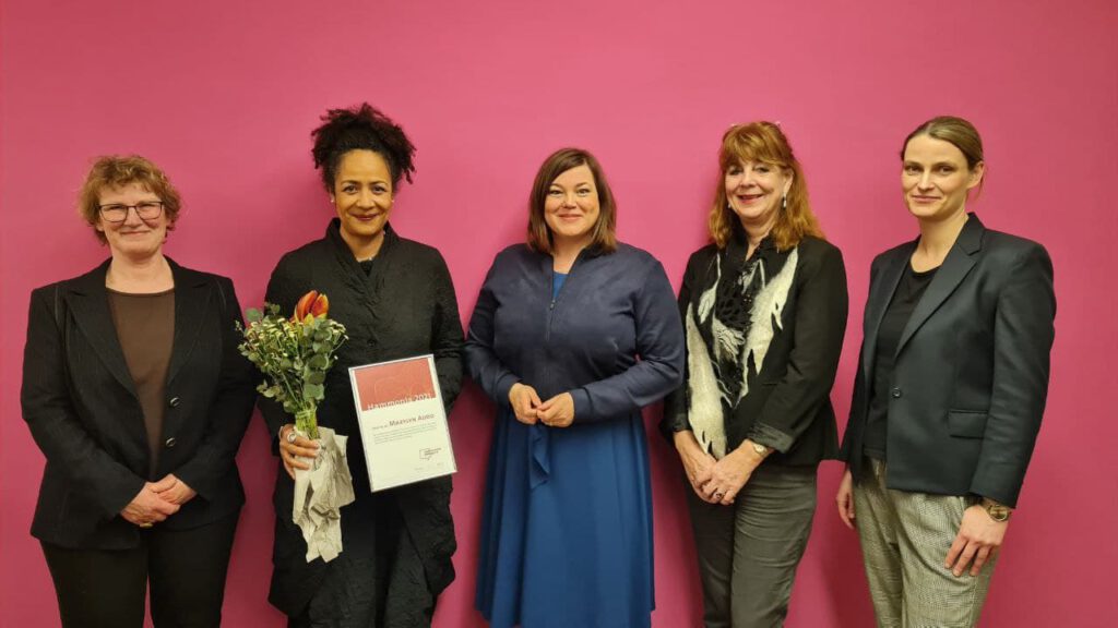 Gruppenfoto von 5 Personen vor pinkfarbener Wand mit Urkunde und Blumenstrauß