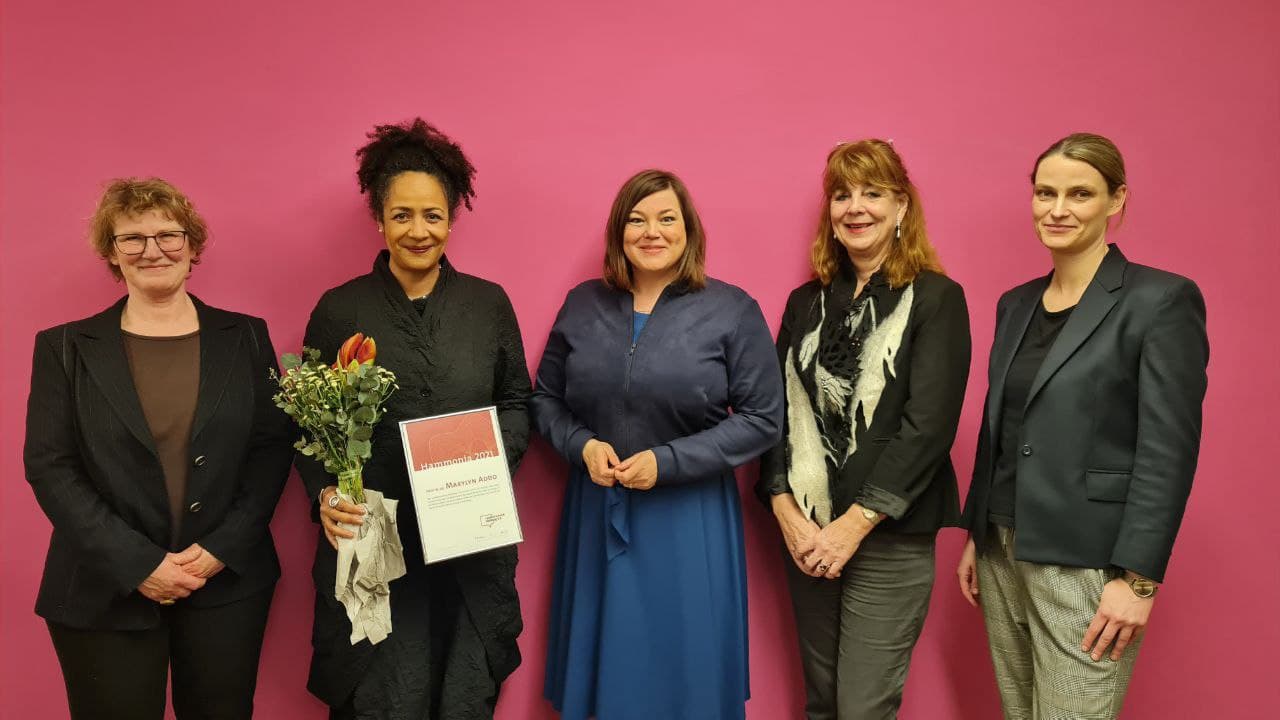 Gruppenfoto von 5 Personen vor pinkfarbener Wand mit Urkunde und Blumenstrauß