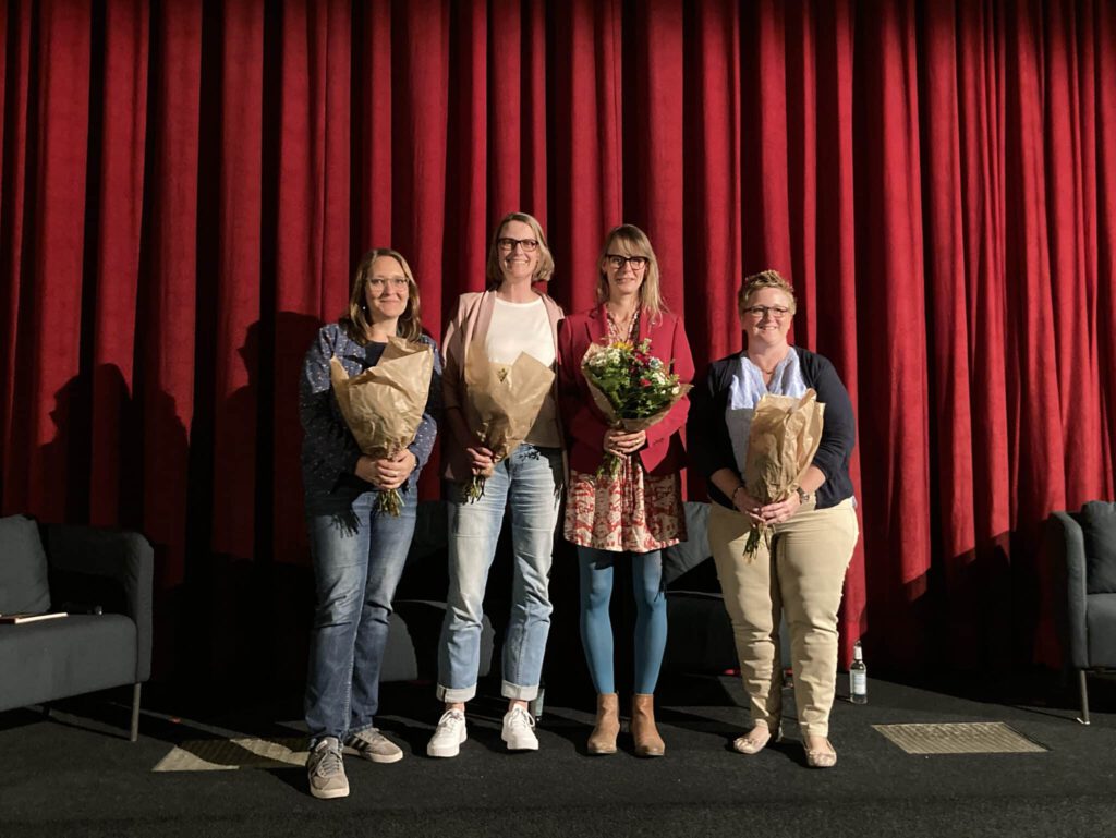 Dr. Christina Maria Huber, Annika Huisinga, Sandra Goldschmidt und Ina von Husen posieren mit Blumenstäußen vor einem Kino Vorhang im Abaton Kino