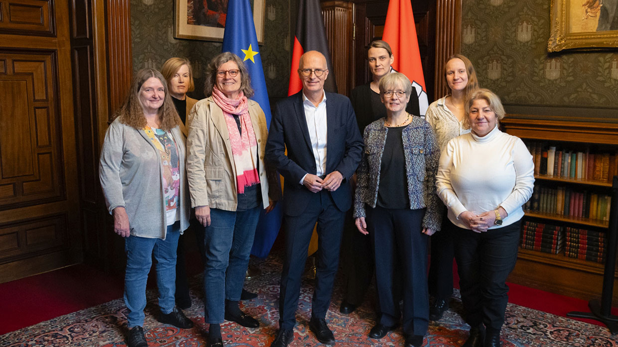 Gruppenfoto im Hamburger Rathaus vor drei Fahnen (EU, Deutschland und Hamburg). Zu sehen sind von links nach rechts: Angelika Ohse, Doris Schramm, Angela Fechner, Peter Tschentscher, Annika Huisinga, Eva Burgdorf, Jarla Wessel und Güler Ulas.