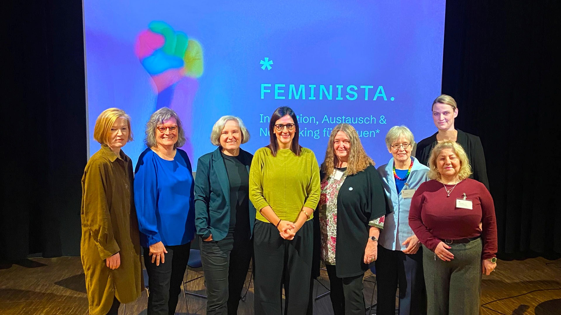 Gruppenbild mit Doris Schramm, Angela Fechner, Franziska Rauchut, Maryam Blumenthal, Angelika Ohse, Eva Burgdorf, Güle Ulas und Annika Huisinga vor einem Beamer-Hintergrund mit dem Plakat der Veranstaltung FEMINISTA.