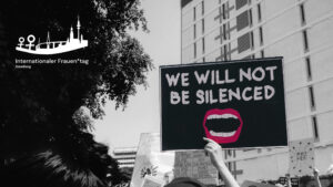 Foto einer Demonstration, auf einem zentral stehenden Schild ist zu lesen "We will not be silenced". In der Ecke des Bildes ist das Logo des Projekts "Frauentag Hamburg" zu sehen.